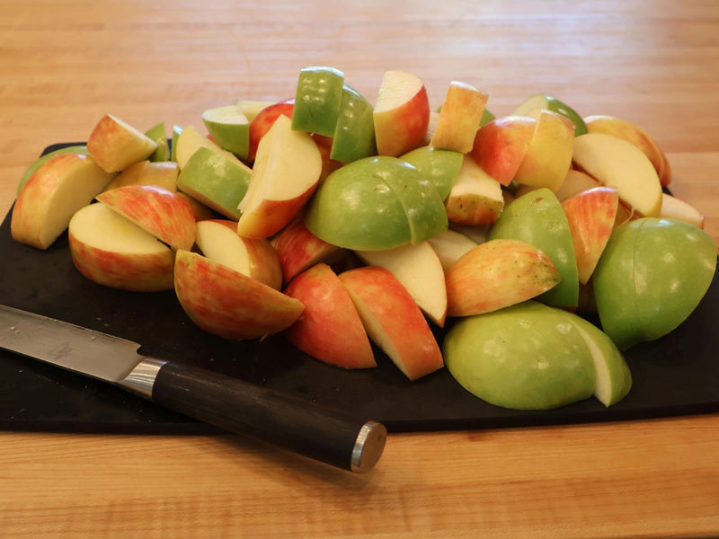 Quartered red and green apples on a cutting board beside a knife