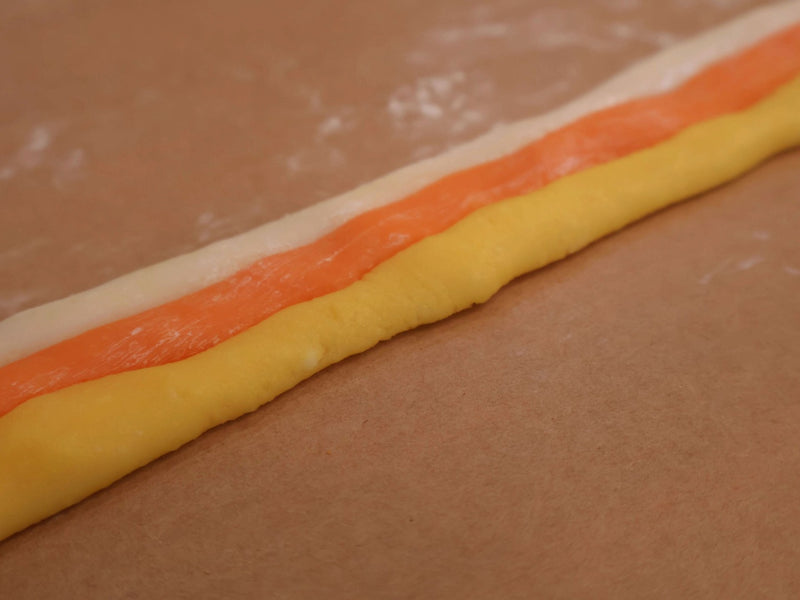 Three-color candy corn dough arranged into strips for cutting