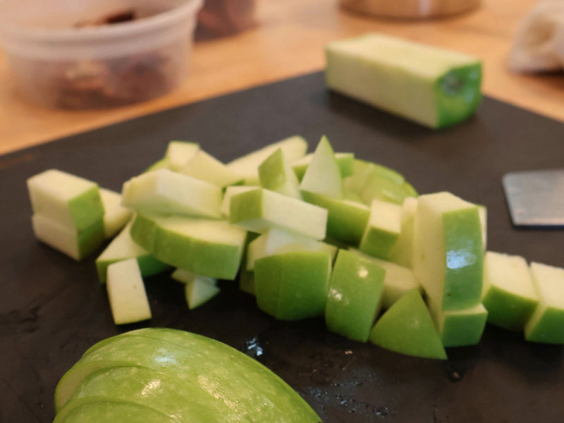 Green apple pieces being chopped on a cutting board for fall bark