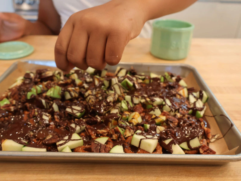 Toppings being added by hand to chocolate fall bark on a baking sheet