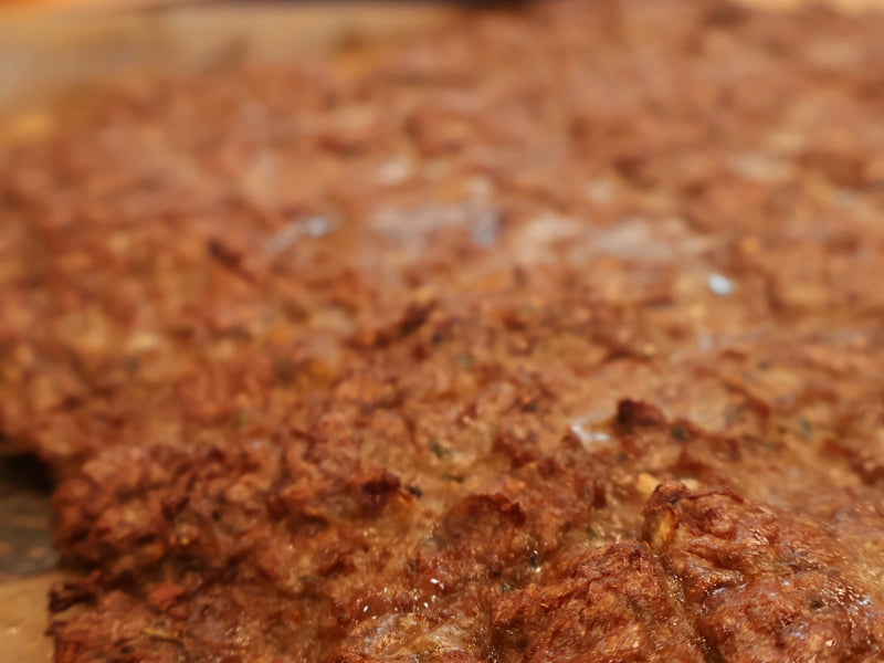 Thin layer of seasoned kebab meat spread across a sheet pan before baking